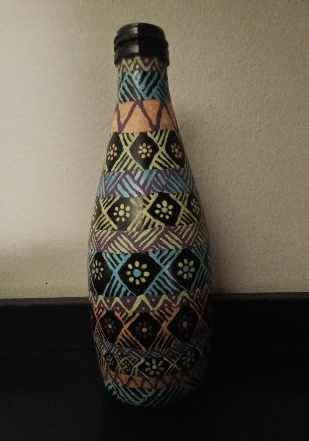 A decorative bottle covered in a colorful geometric tribal-style pattern of blue, yellow, pink, green, and orange.