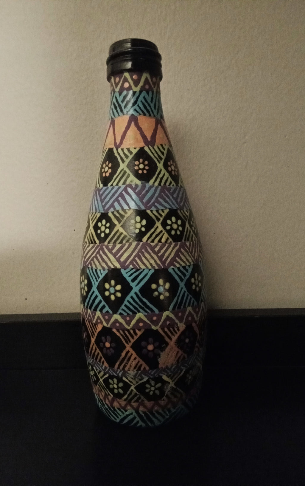 A decorative bottle covered in a colorful geometric tribal-style pattern of blue, yellow, pink, green, and orange.